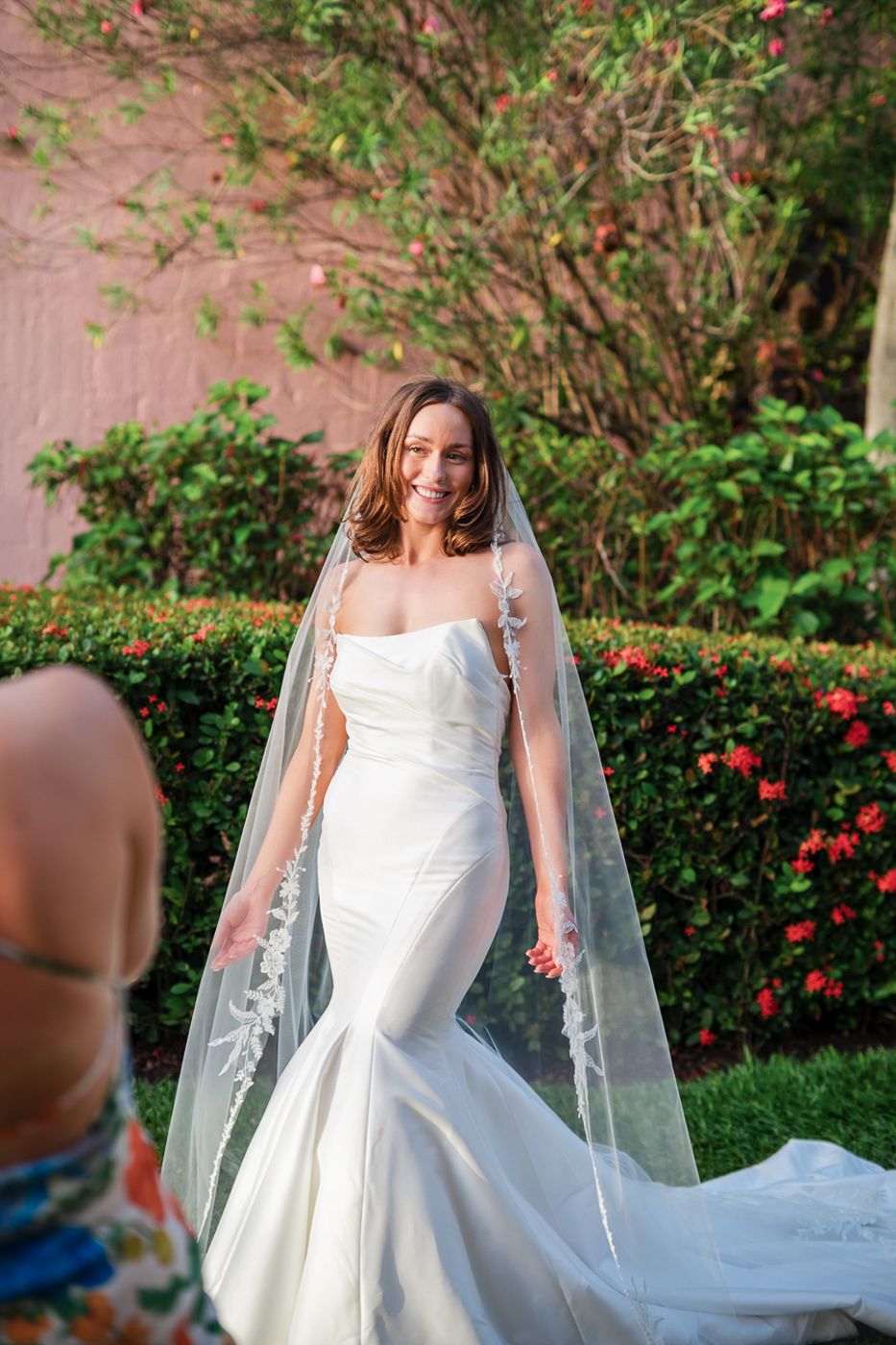 A beautiful bridal portrait showcasing a mermaid wedding dress and veil against a floral garden backdrop.