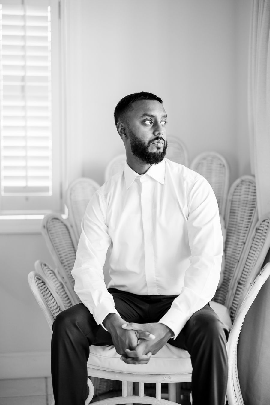Portrait of person in white dress shirt sitting thoughtfully on rattan chair.