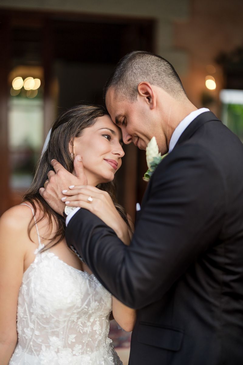 Bride and groom share an intimate moment, foreheads touching, as groom gently cups her face at their wedding.