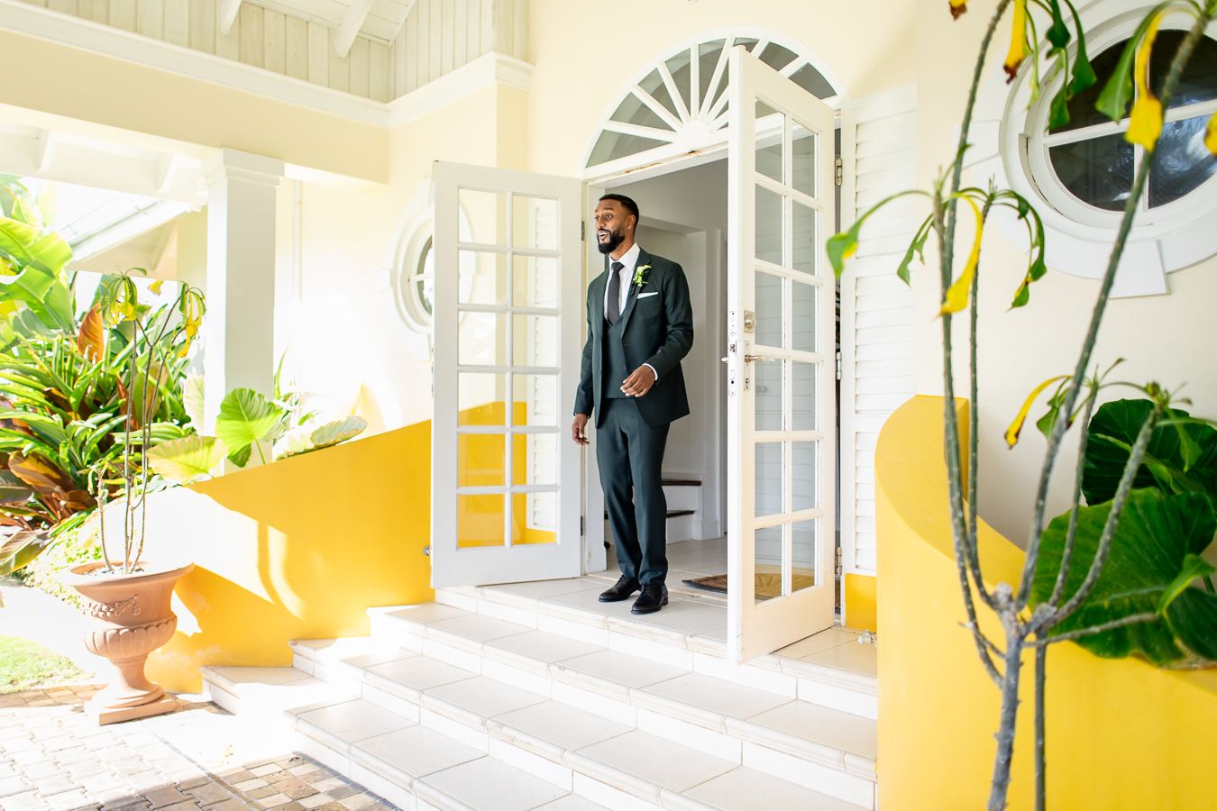 Yellow-walled veranda with potted plants and white architectural details in tropical setting.