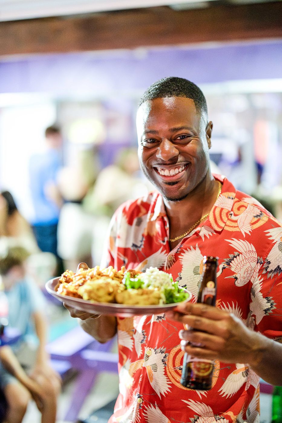 Person in coral Hawaiian shirt holding a plate of food and smiling at a casual dining event. Oistins fish fry barbados