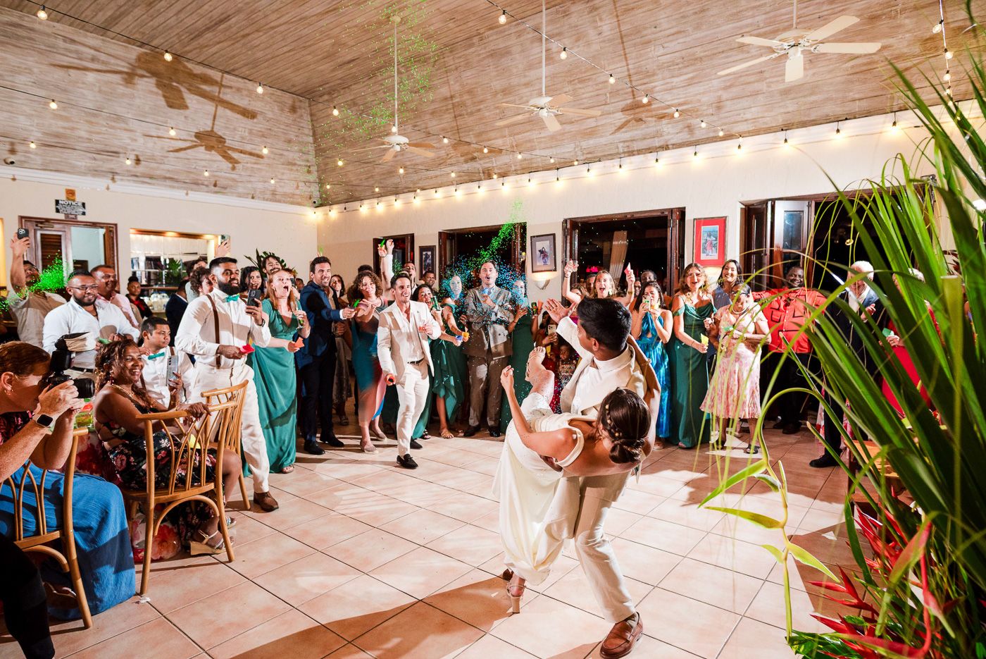 Couple performs spectacular dance lift during wedding reception with guests cheering.