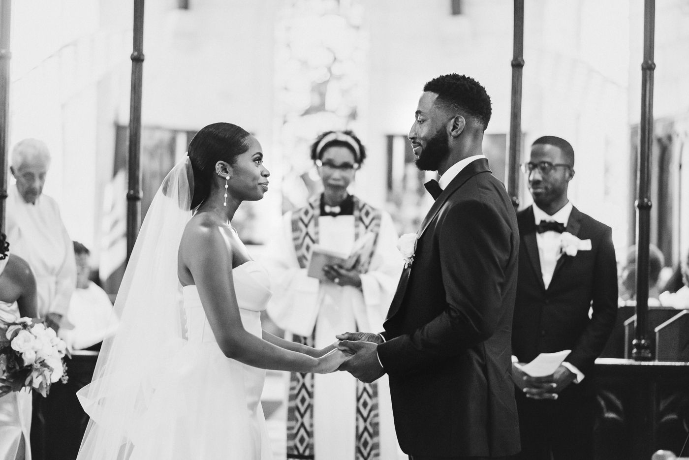 Black and white photo of wedding ceremony exchange at ornate church altar.