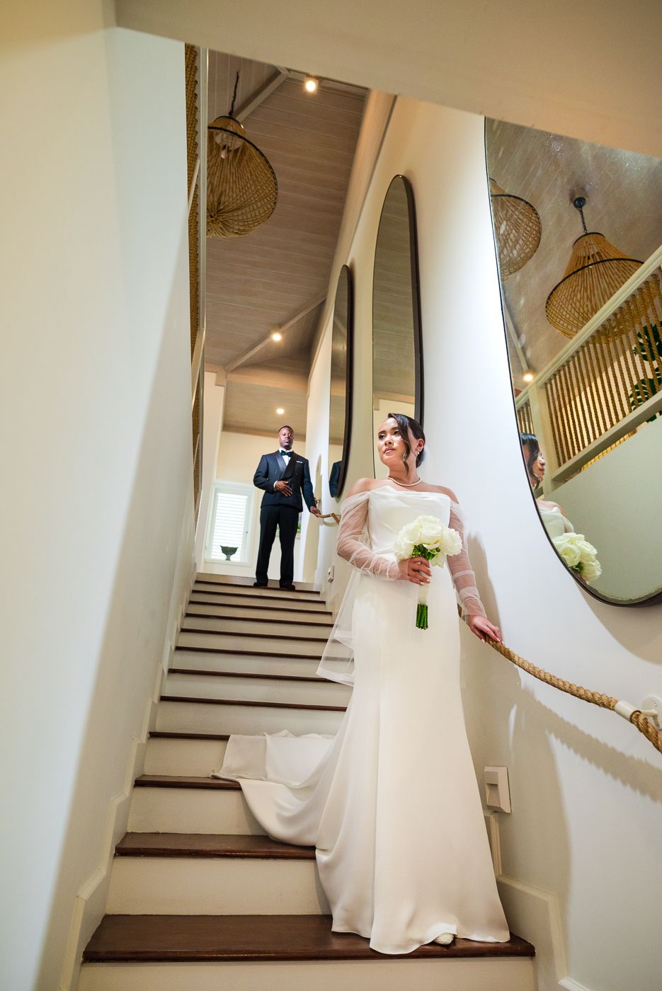Elegant wedding photo on white staircase with architectural details and oval mirror.