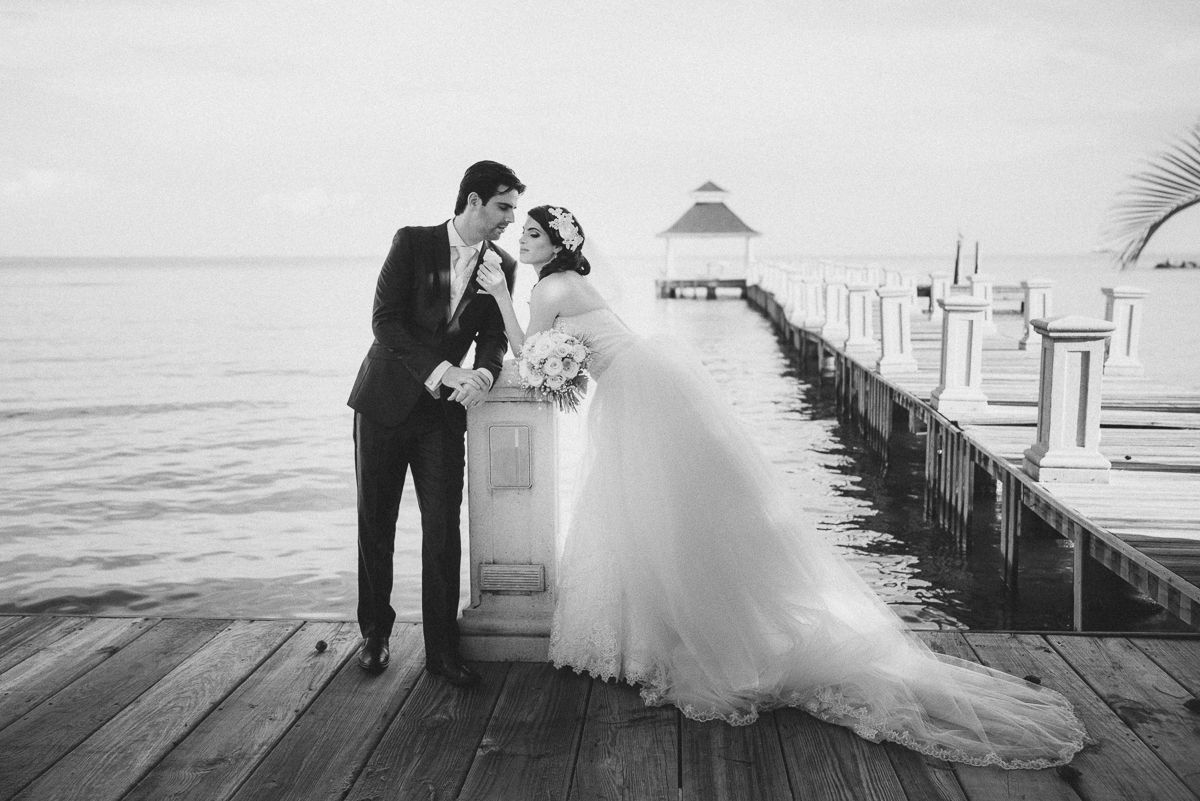 Elegant wedding couple posing on wooden pier with water views in black and white.