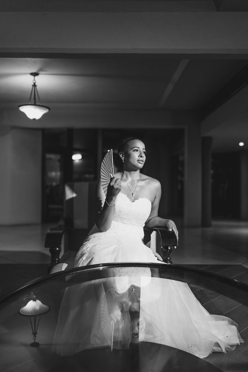 Black and white photo of a bride in a strapless gown holding a fan, posing elegantly indoors at night.