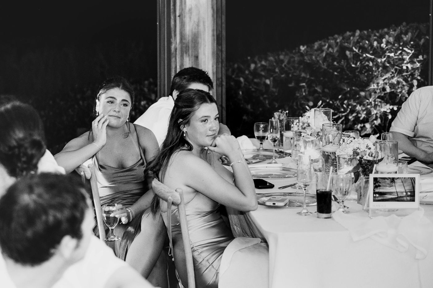 Black and white wedding reception photo of elegantly dressed guests seated at a decorated dinner table.