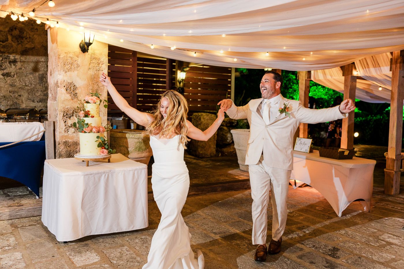 Bride and groom share joyful first dance at elegant outdoor wedding reception with draped ceiling lights.