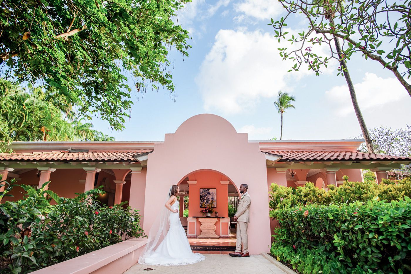 Pink Spanish colonial architecture with terra cotta roof tiles and tropical landscaping.