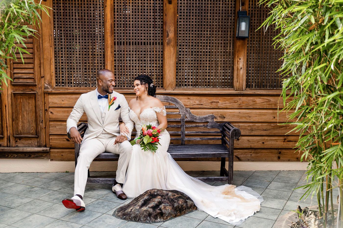 Couple shares an intimate moment on a wooden bench surrounded by lush bamboo in an Asian-inspired garden setting.
