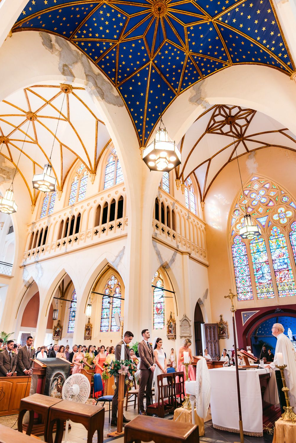 Elegant church interior with stained glass windows and blue starry ceiling adorned with gold stars and white columns.