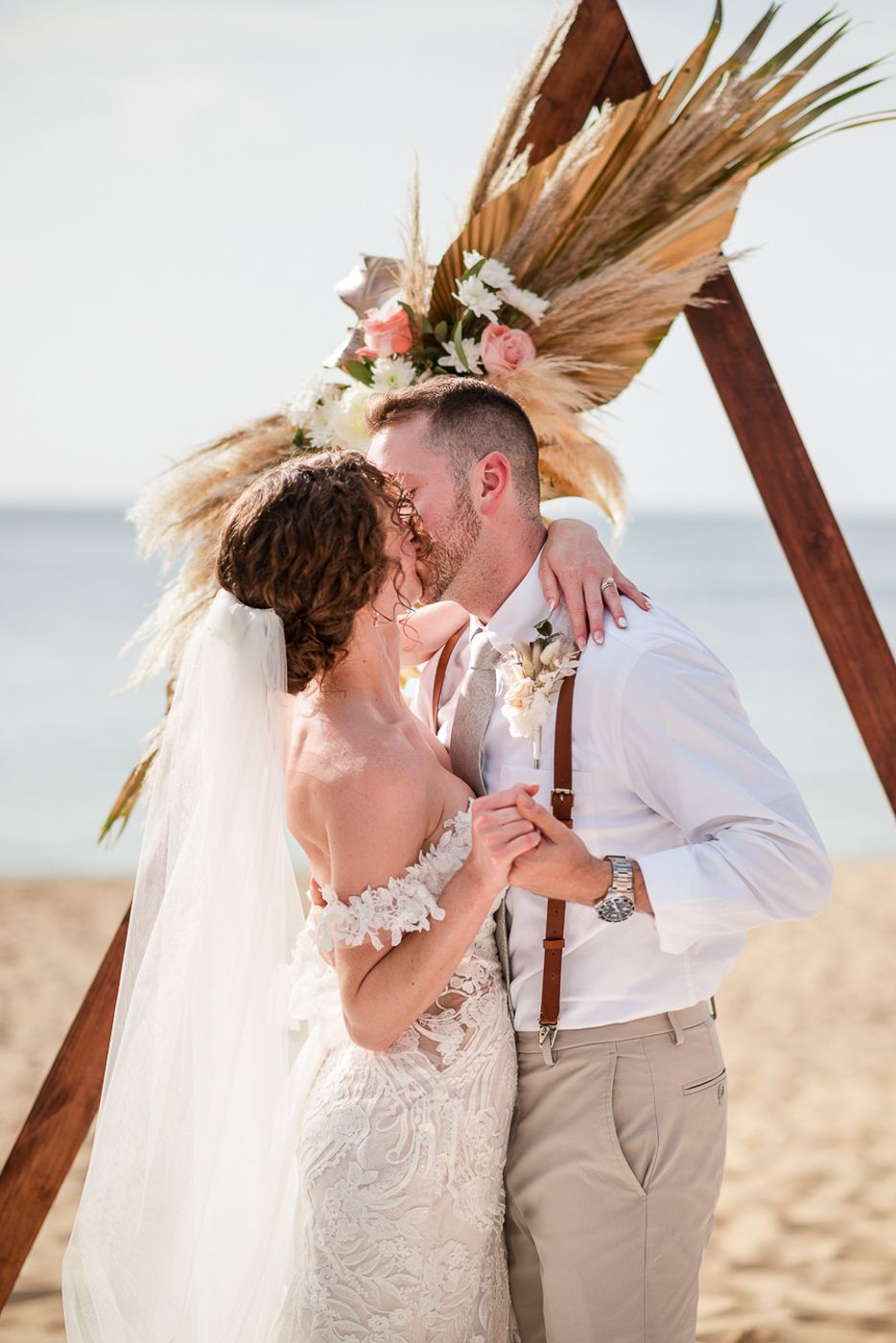 Intimate beach wedding portraits with dried palm decor and soft golden lighting.