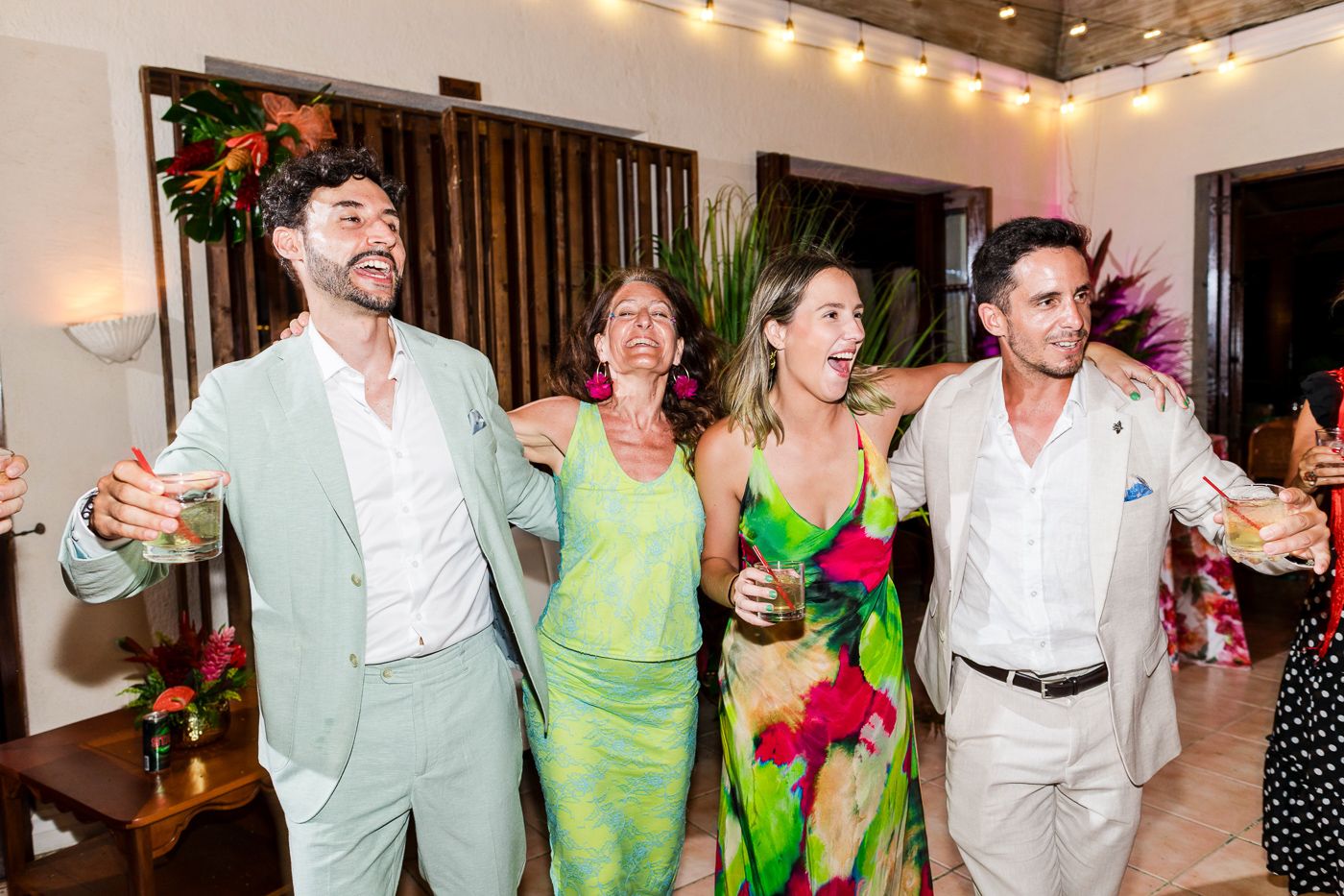 Large group of wedding guests in green and white attire dance together at an indoor celebration.