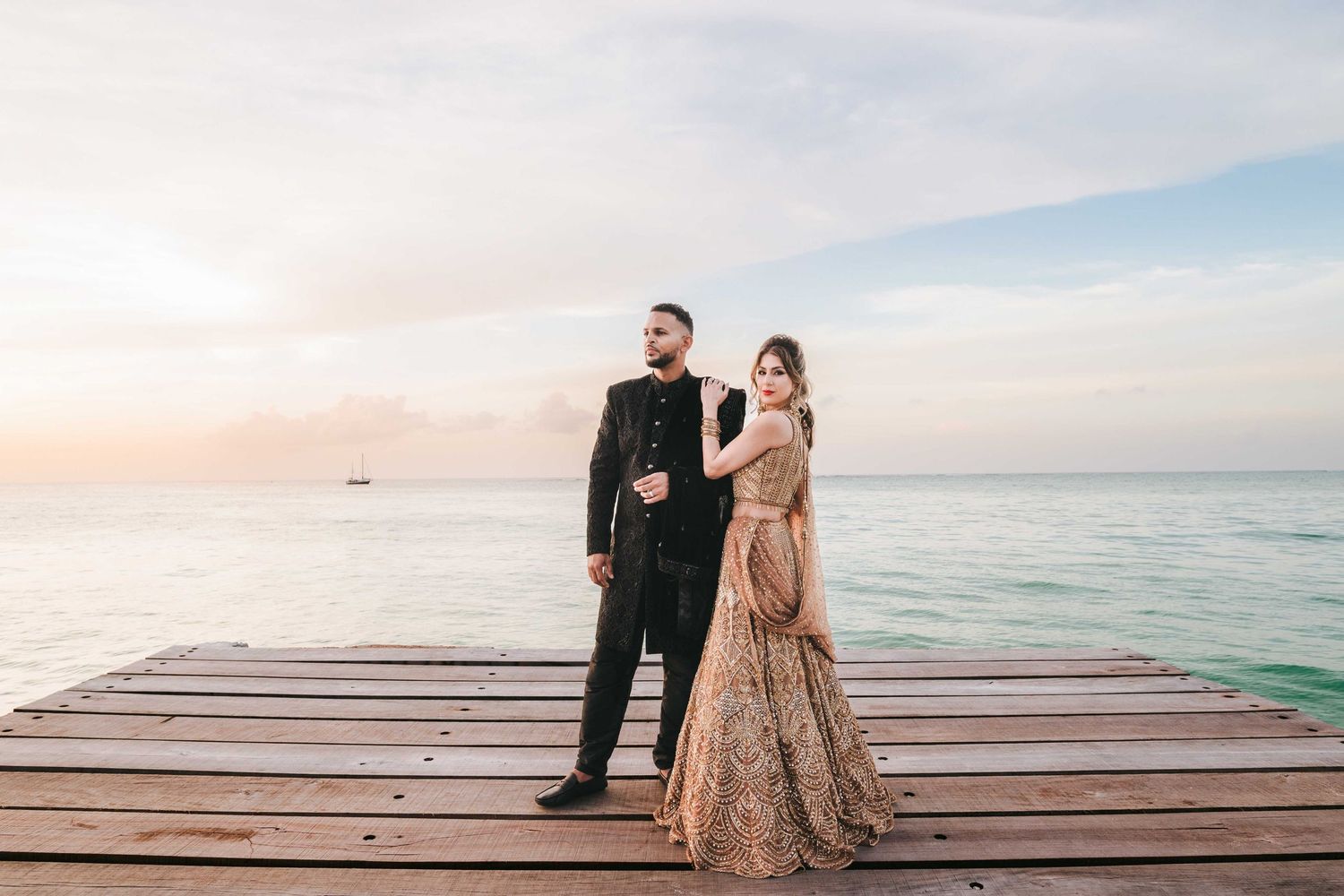 Elegant couple stands on oceanfront pier at sunset in formal evening attire.