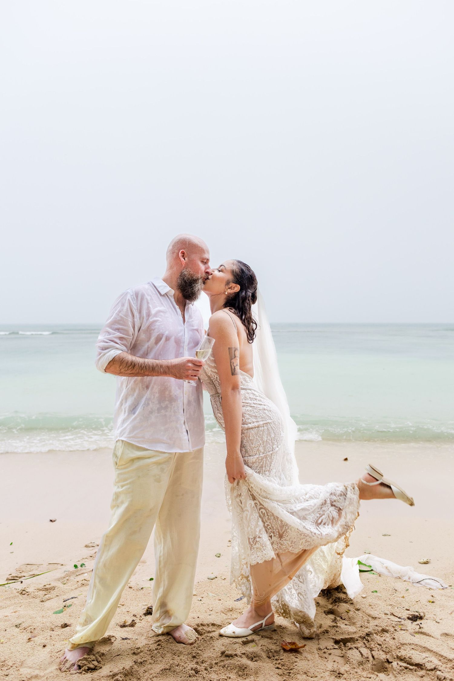 Couple sharing a romantic kiss on a sandy beach during their destination wedding ceremony by the ocean.