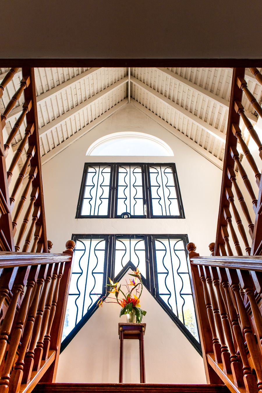 Grand staircase with wooden banisters leading to ornate arched windows and vaulted ceiling in elegant interior.