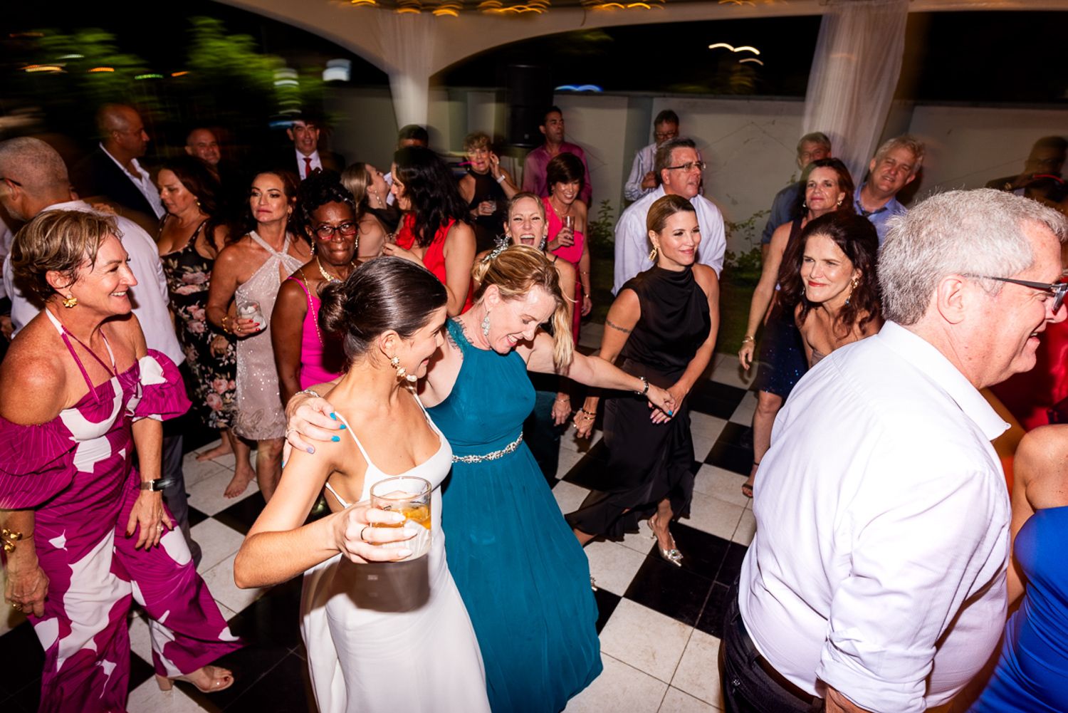 Wedding guests enjoying themselves while dancing on a black and white checkered dance floor at a reception celebration.