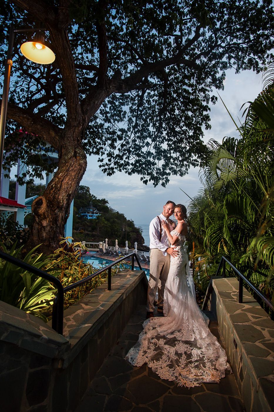 Evening wedding portrait on a stone pathway with dramatic lighting and tropical foliage.