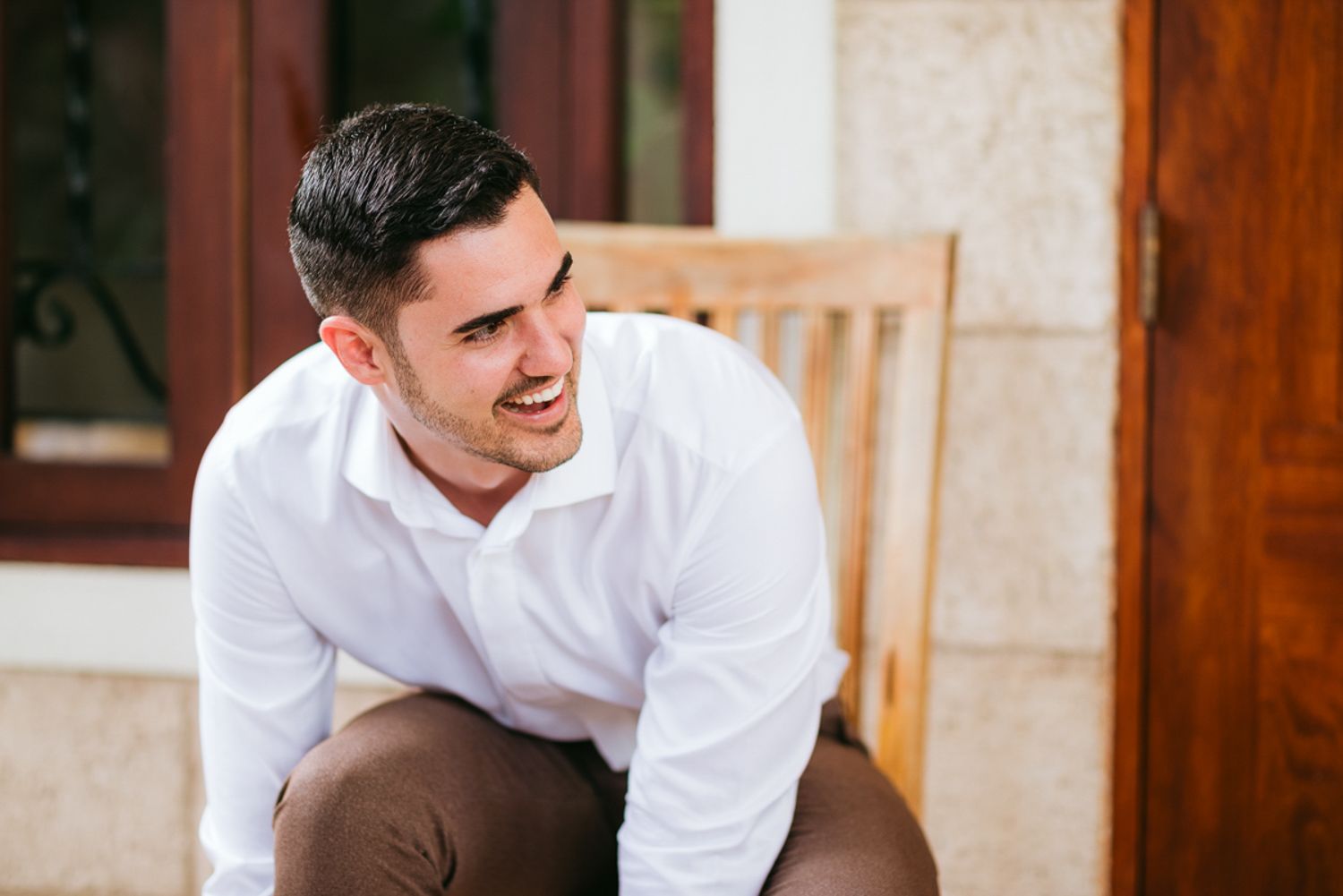 Young man in white dress shirt laughing while standing on outdoor stone staircase.