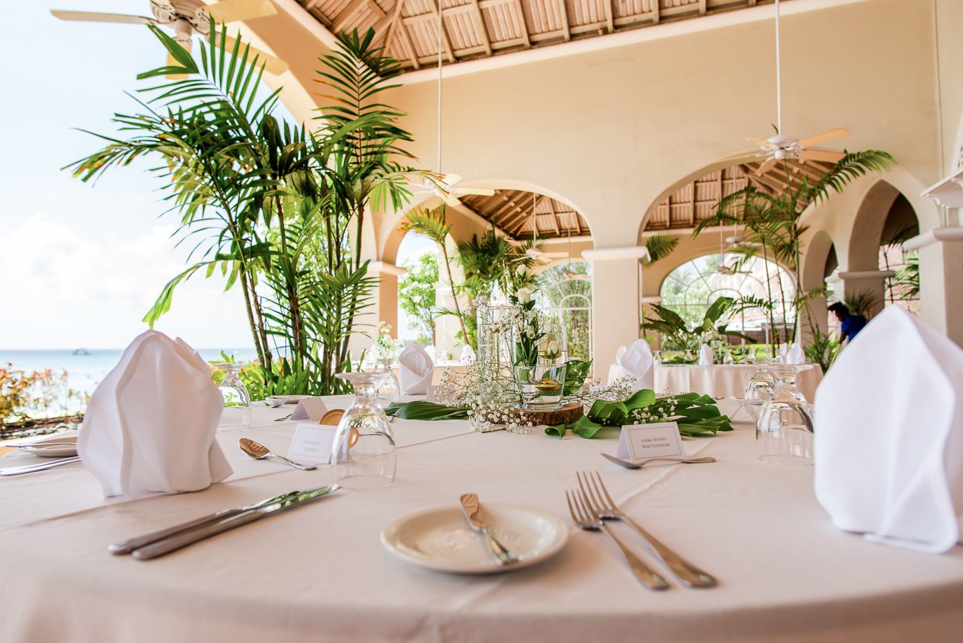 Tropical dining setup with white linens and palm fronds under vaulted bamboo ceilings.