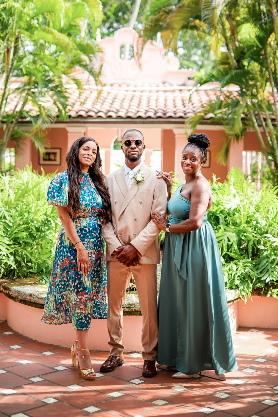 Wedding party in colorful dresses and beige suit posing in tropical garden setting.