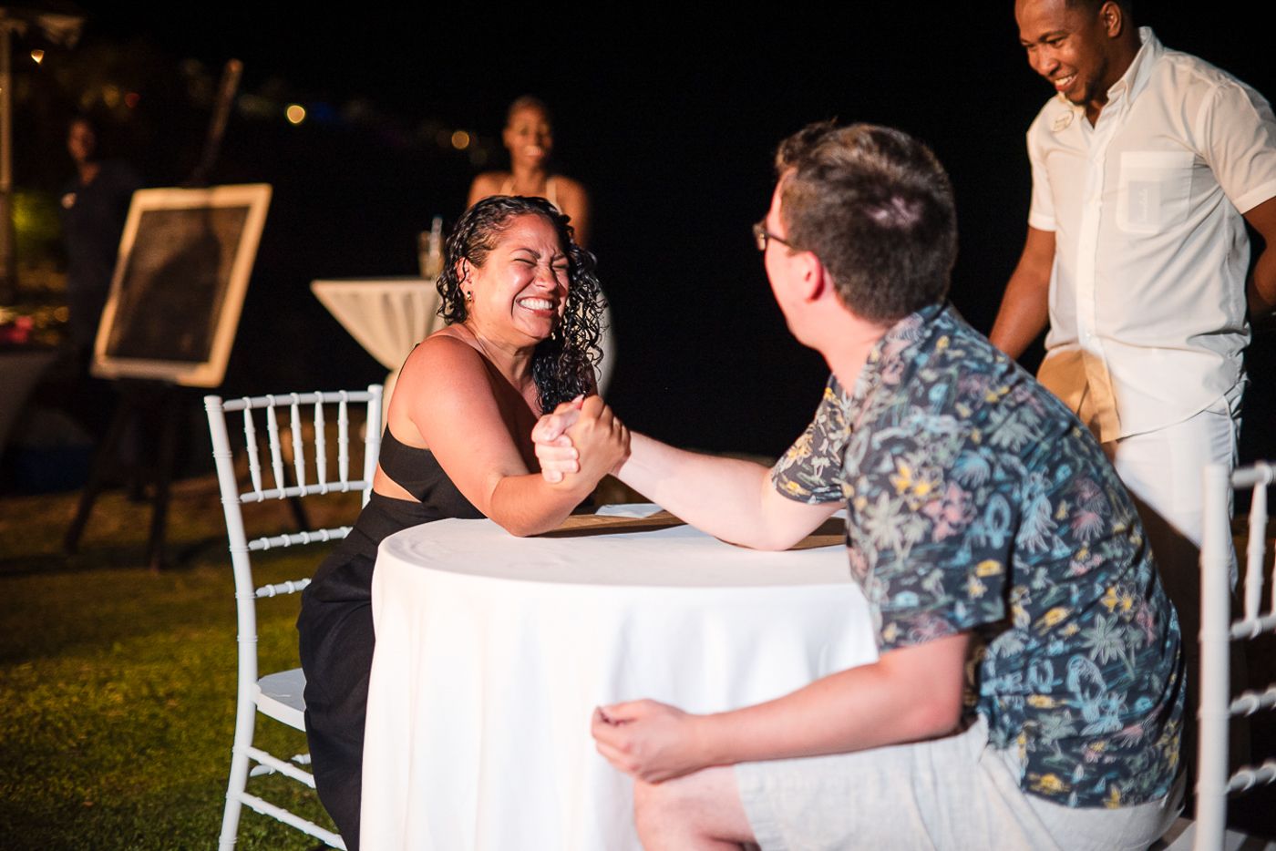 Two people engaged in an intense arm wrestling match at a white clothed table.