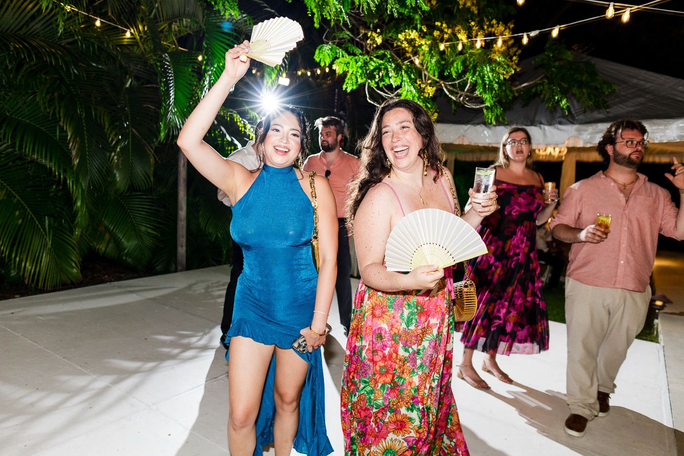 Party guests dance and socialize on a white dance floor surrounded by tropical greenery.
