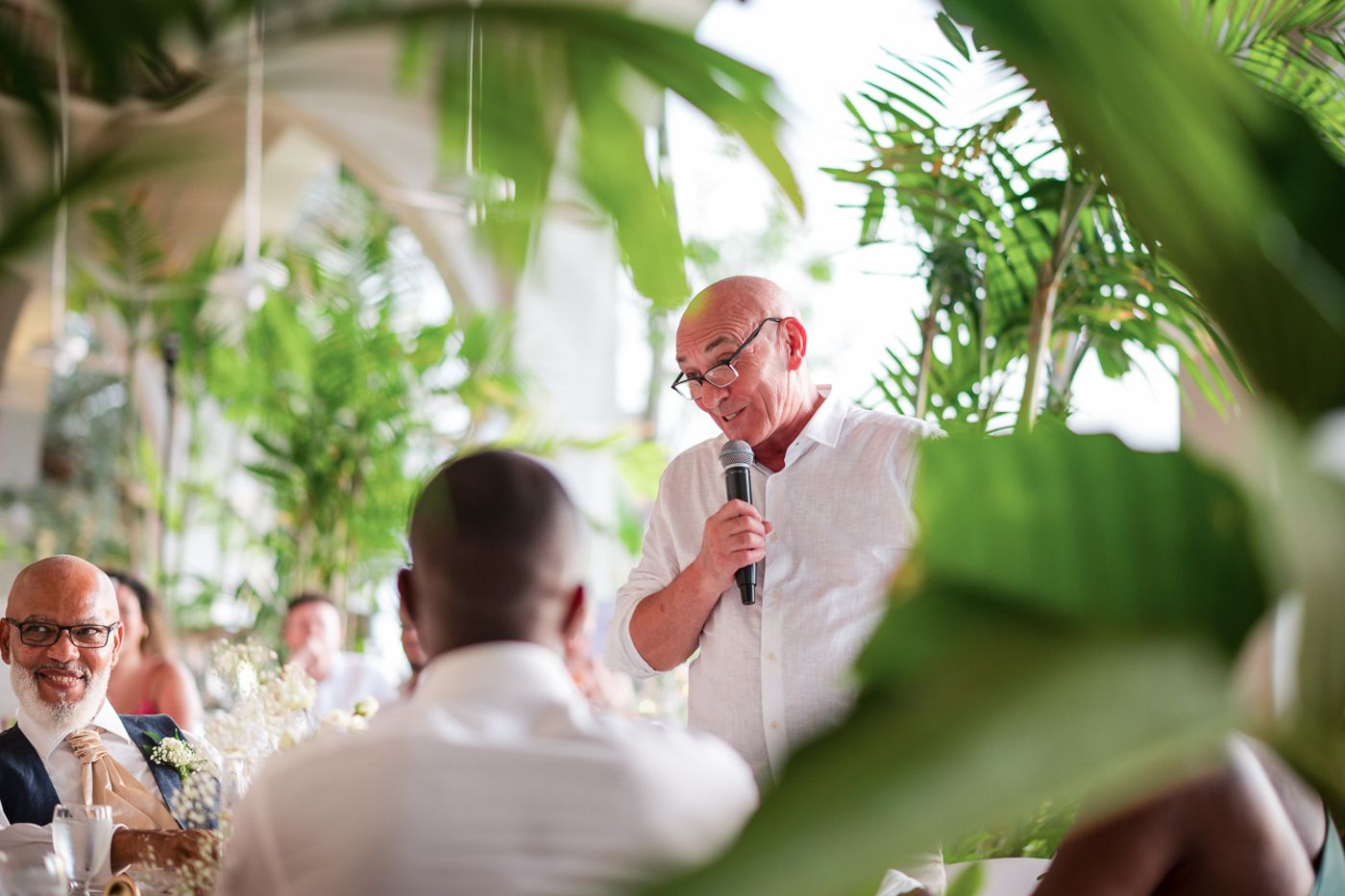 A wedding reception speech in a tropical venue with lush greenery and palm plants decorating the space.