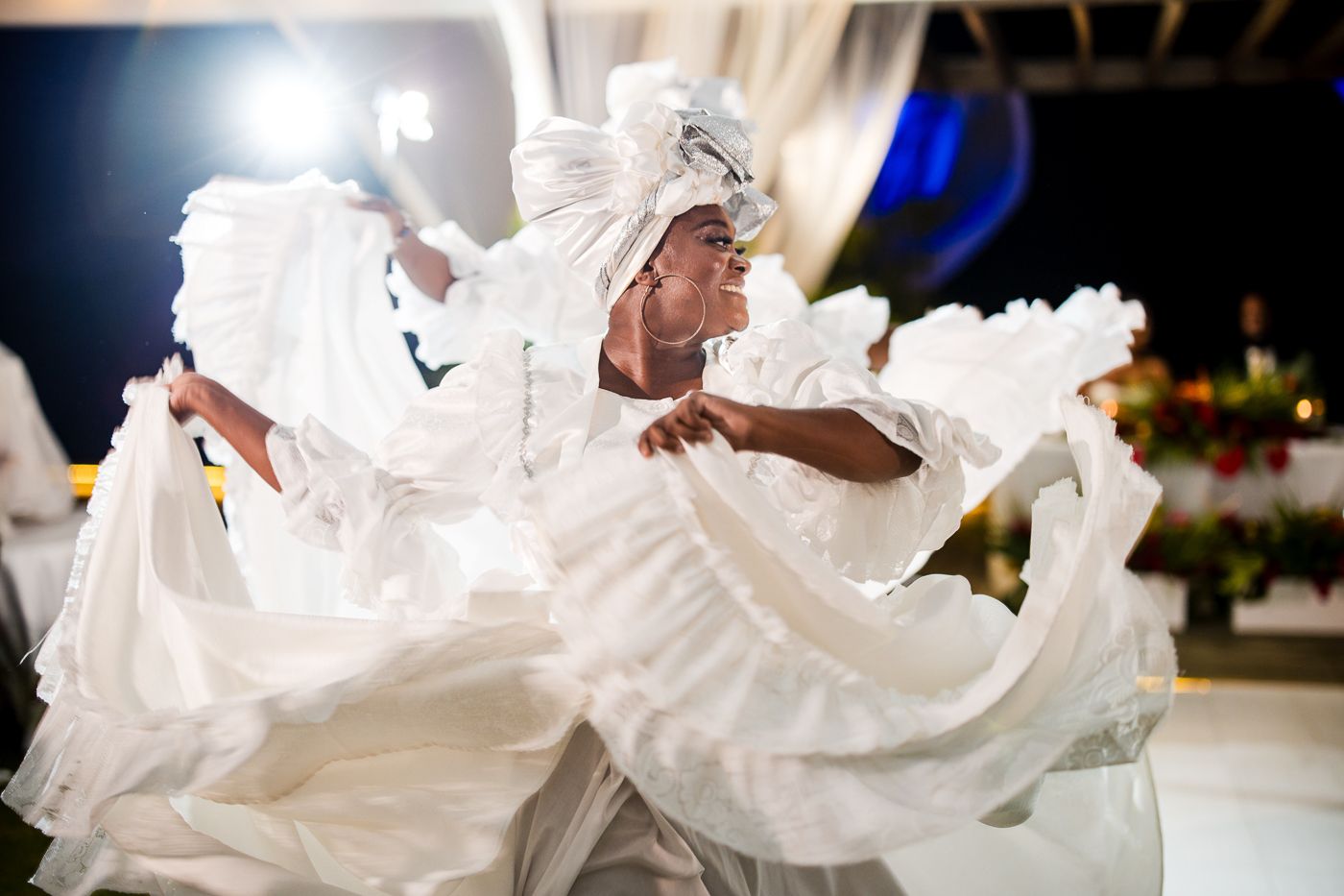 Performer in flowing white dress and headpiece dancing gracefully at a cultural celebration event.
