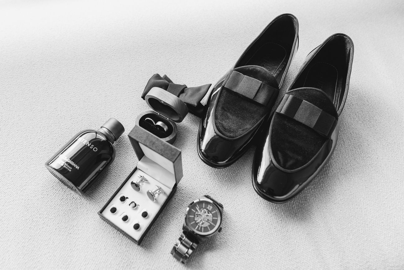 Black and white close-up of dress shoes and accessories arranged for a wedding day.
