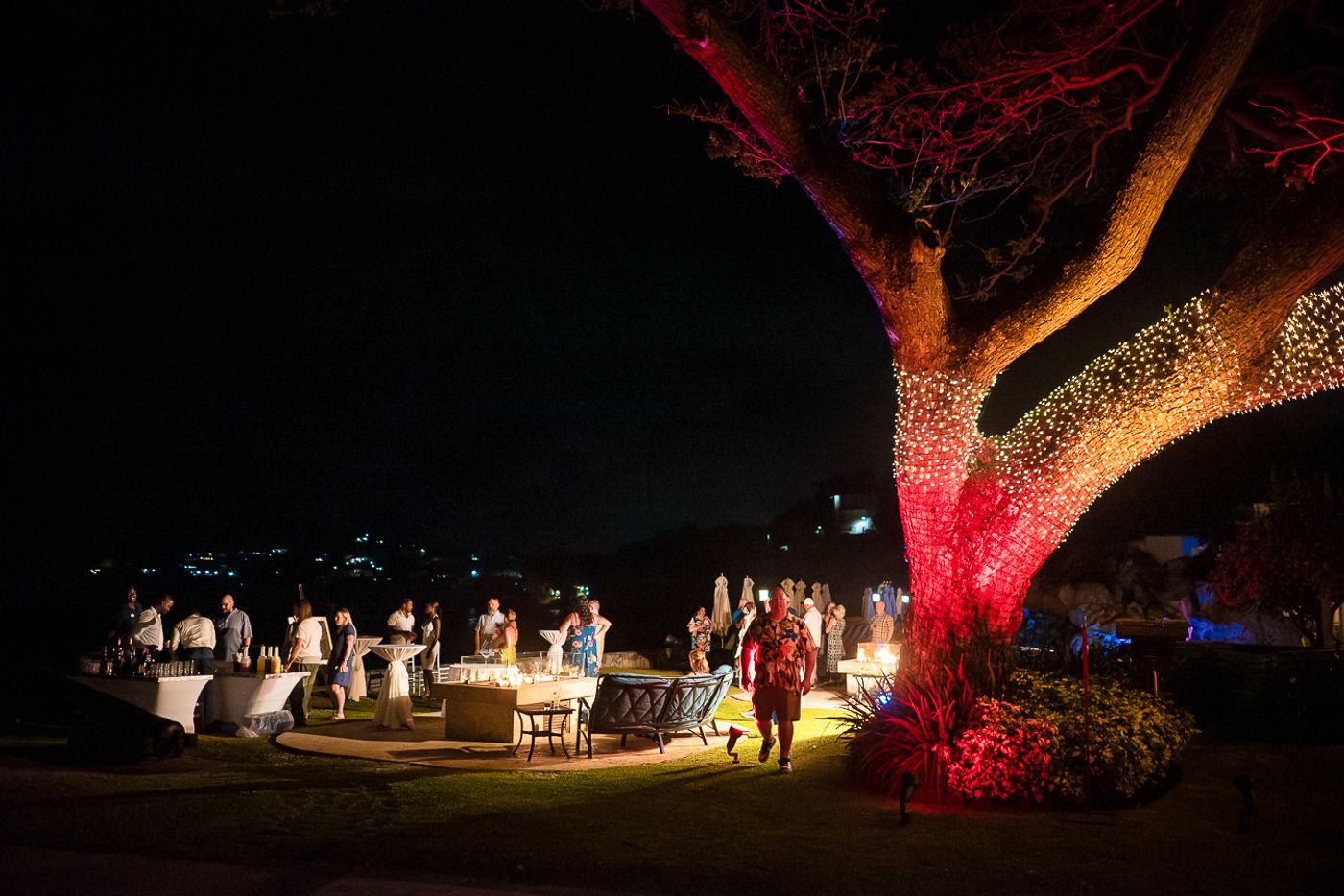 Illuminated tree glows red over an outdoor evening event with white tables and chairs.