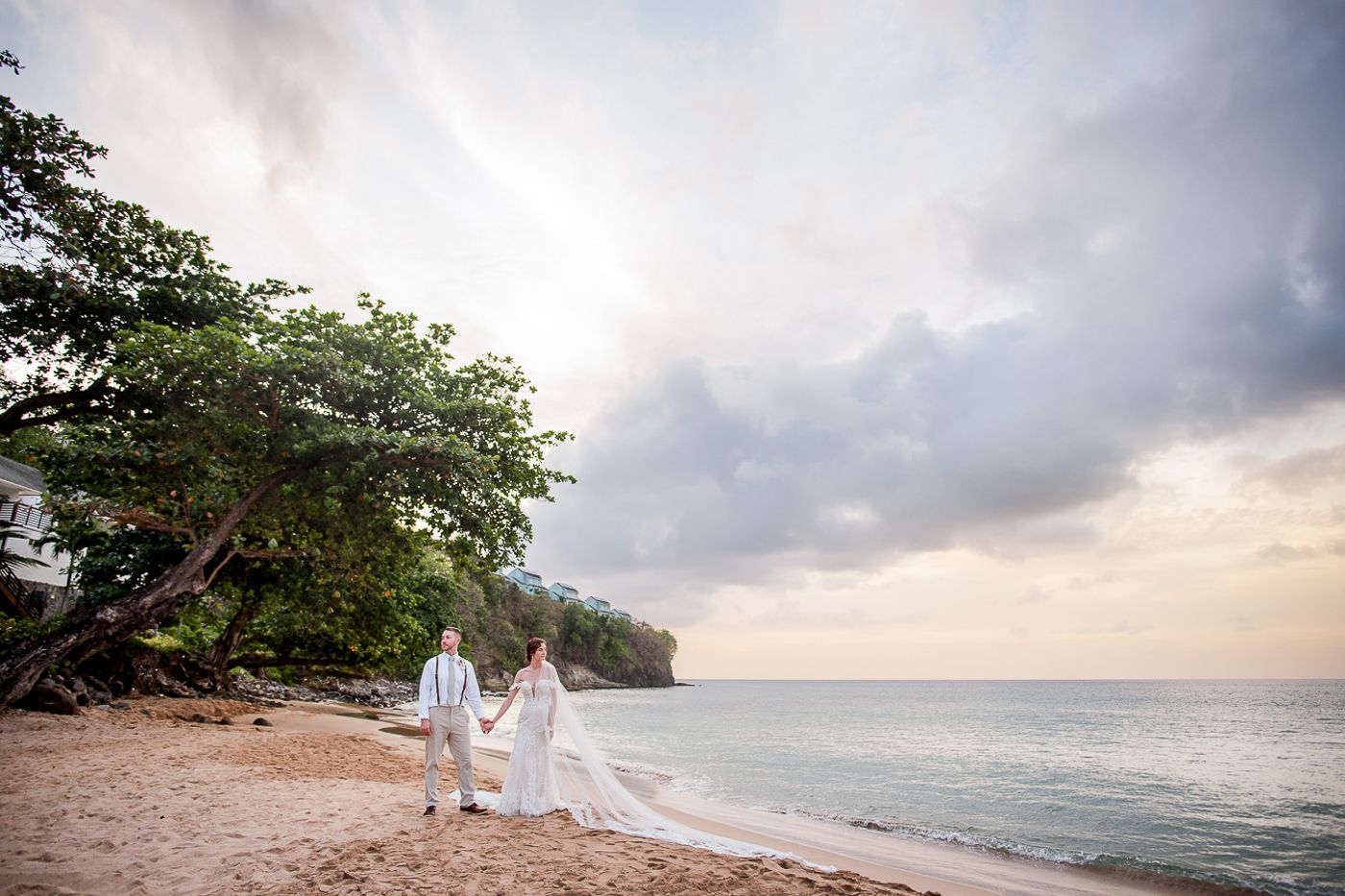 Romantic beach wedding scene at sunset with flowing white dresses against the ocean backdrop.