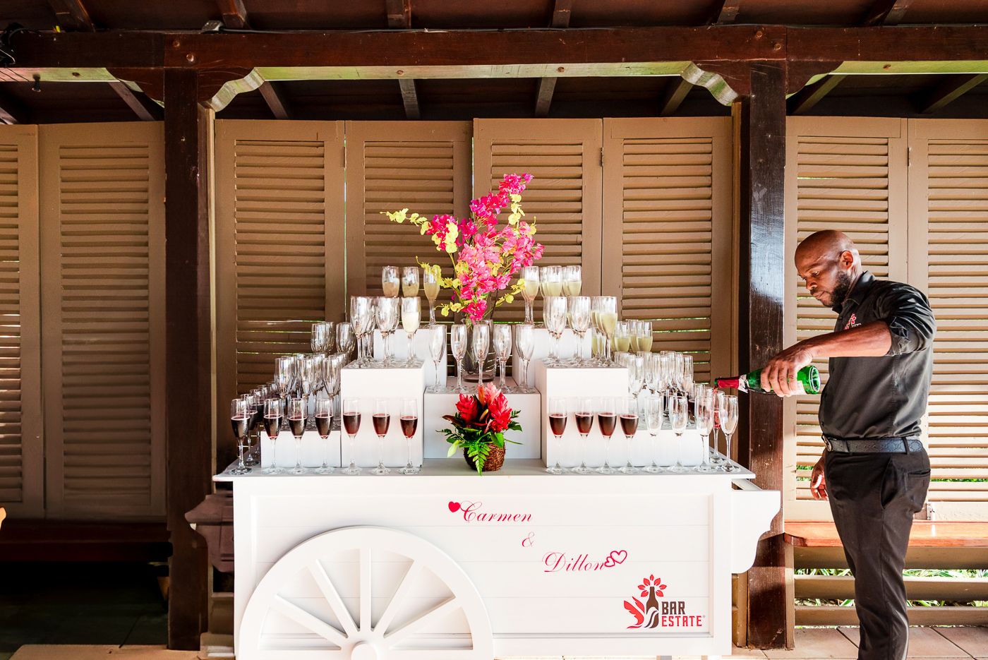 Elegant drink station with pink floral arrangements and champagne glasses at a tropical wedding reception.