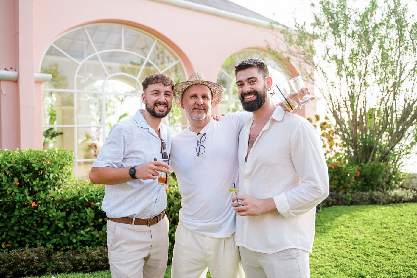 Three friends in casual white attire pose together under an arched entryway.