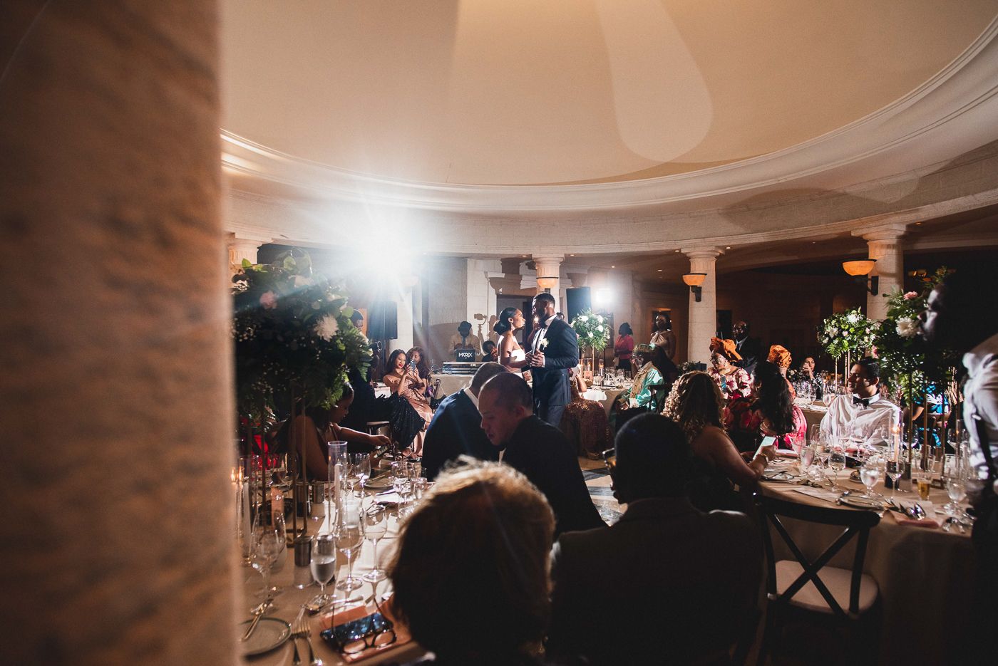Indoor wedding reception with warm ambient lighting and guests gathered at dining tables.