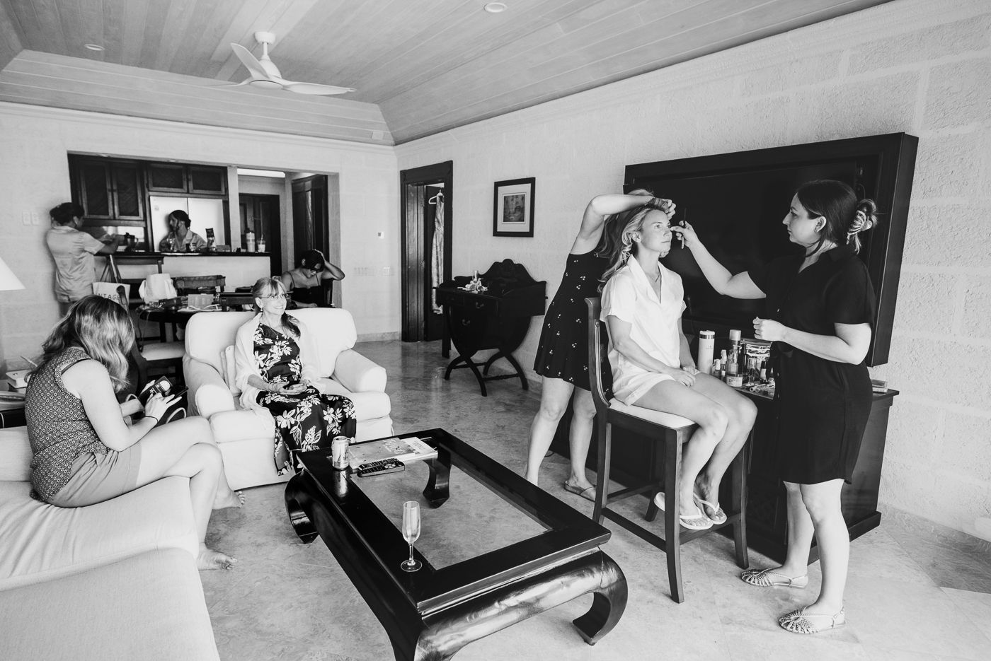 Black and white photo of bride getting hair and makeup done by stylists in a elegant room before her wedding.