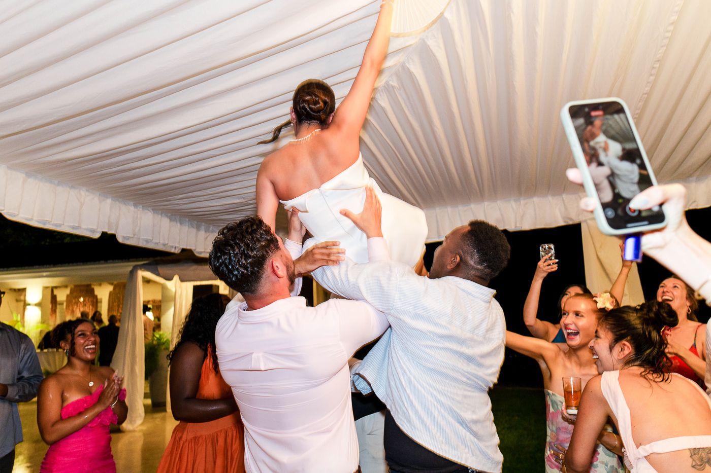 Wedding party dancing under a white tent with dramatic lighting effects.