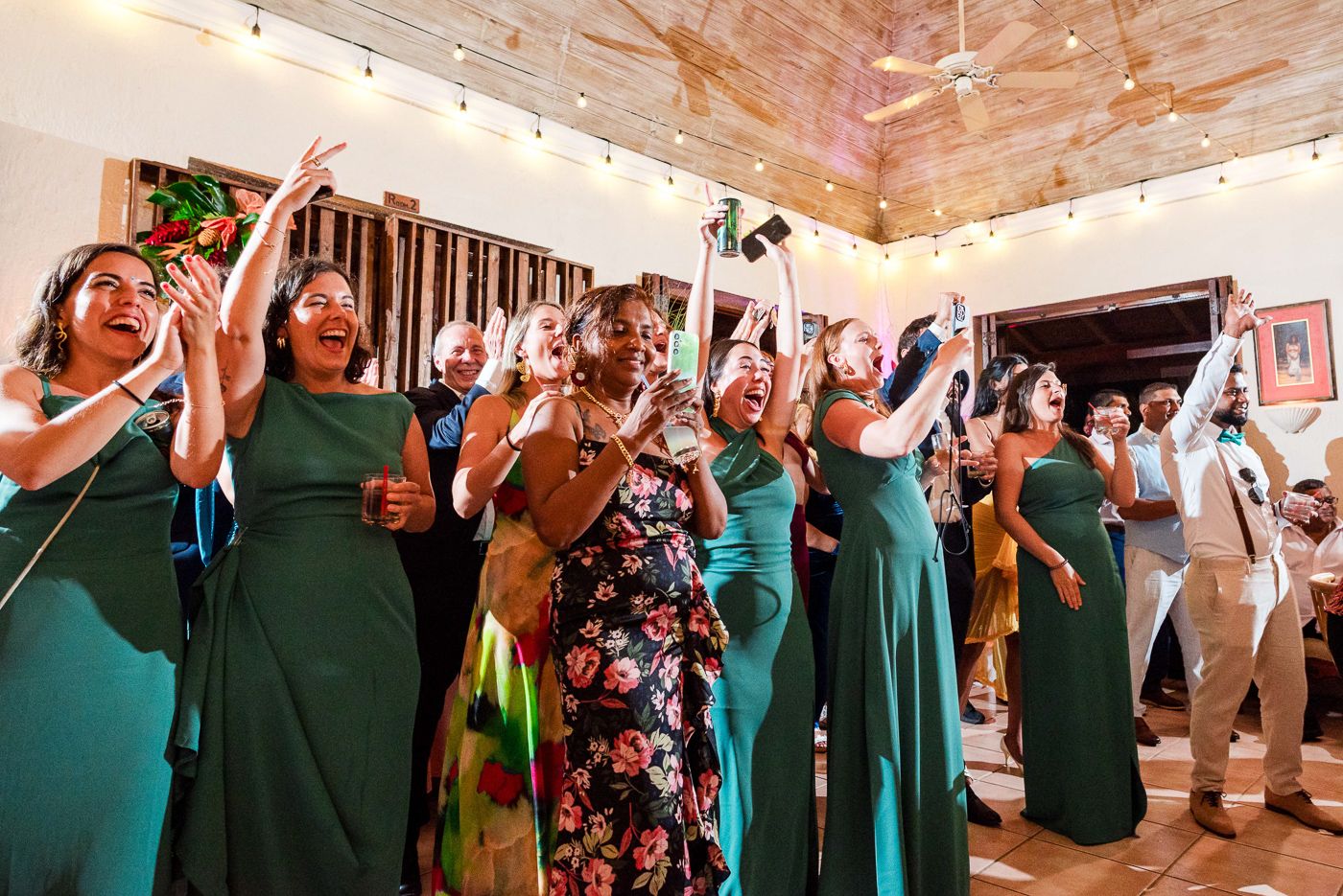 Wedding party in green dresses celebrates enthusiastically during reception festivities.