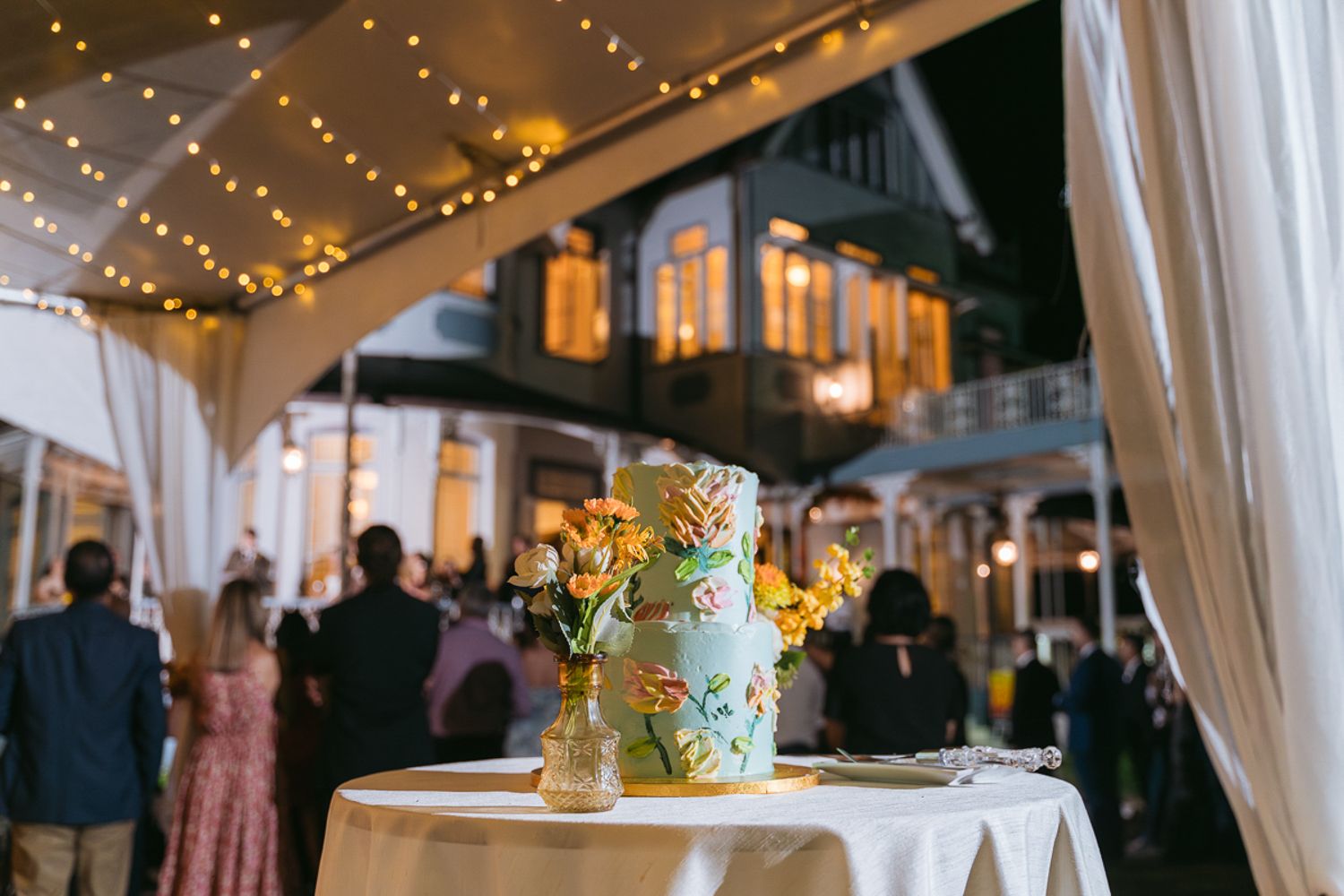 Elegant wedding reception venue with string lights, sheer white drapes, and floral centerpieces on dining tables.