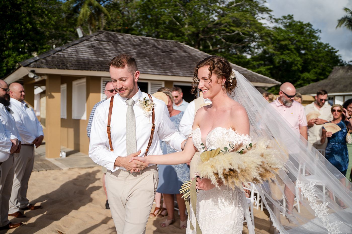 Beachside wedding celebration with guests in light summer attire and palm trees in background.