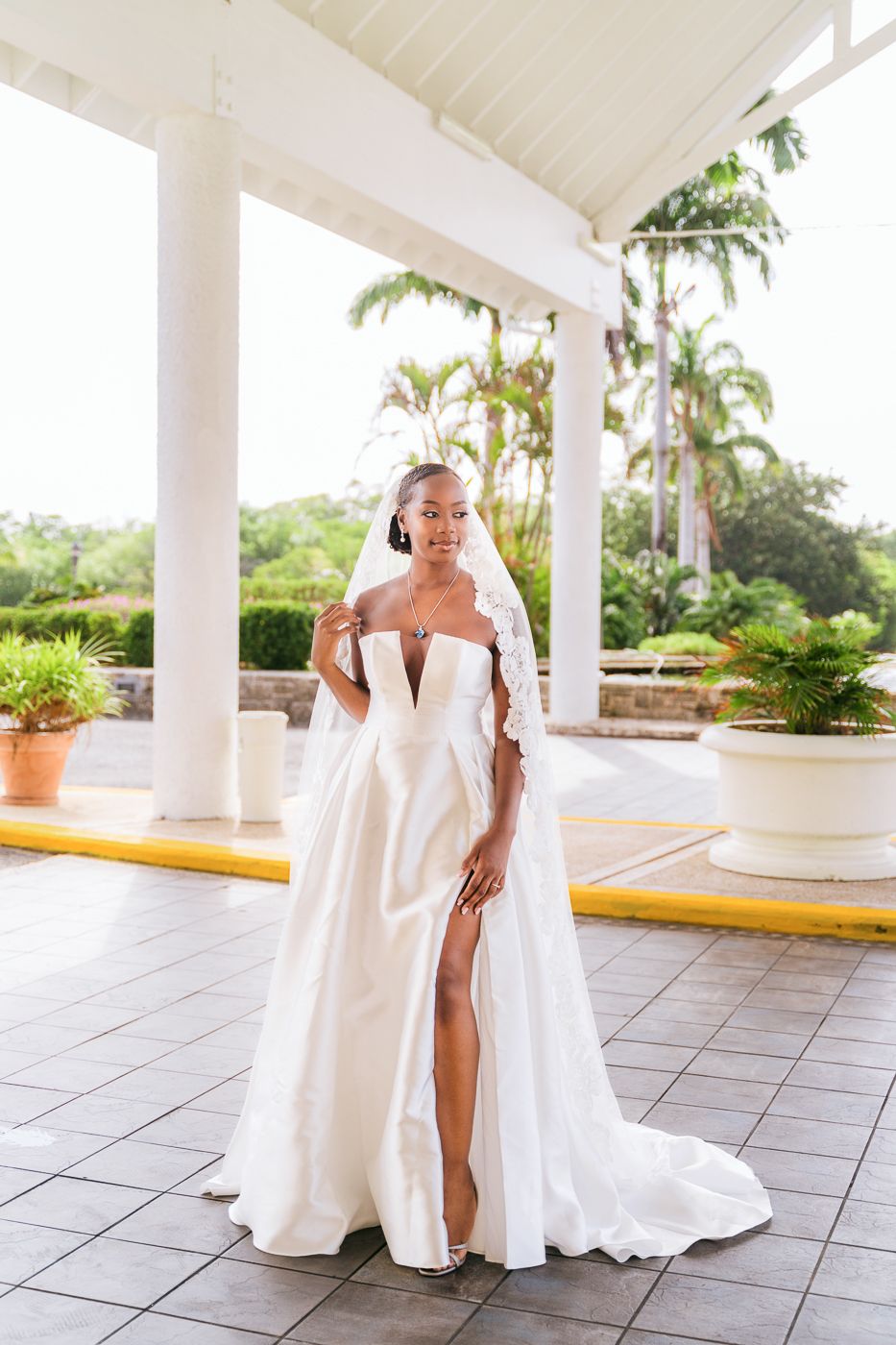 Elegant bride in white off-shoulder wedding gown with high slit poses under columned portico.