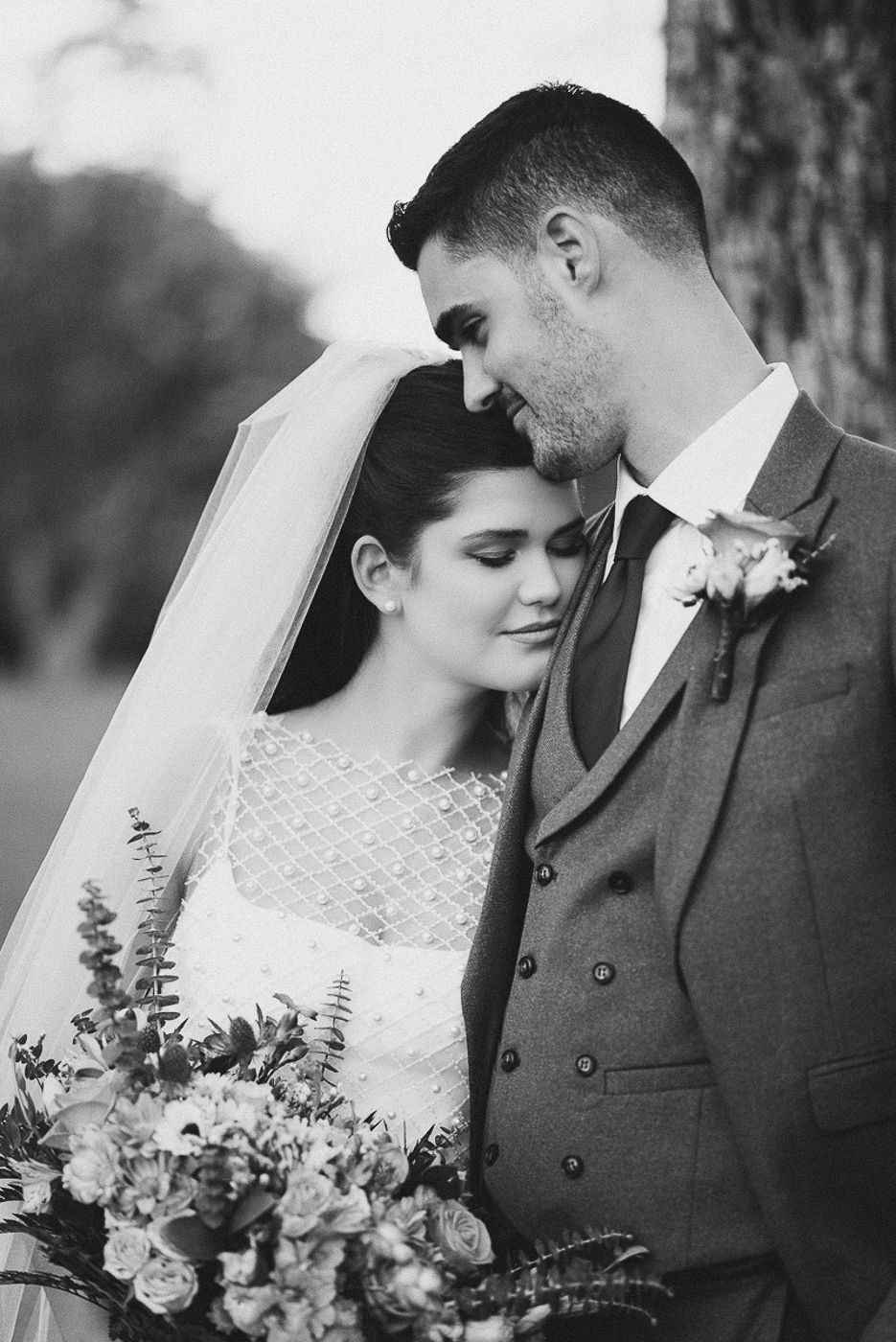 Black and white wedding portrait of bride and groom sharing a tender moment, bride holding a floral bouquet.