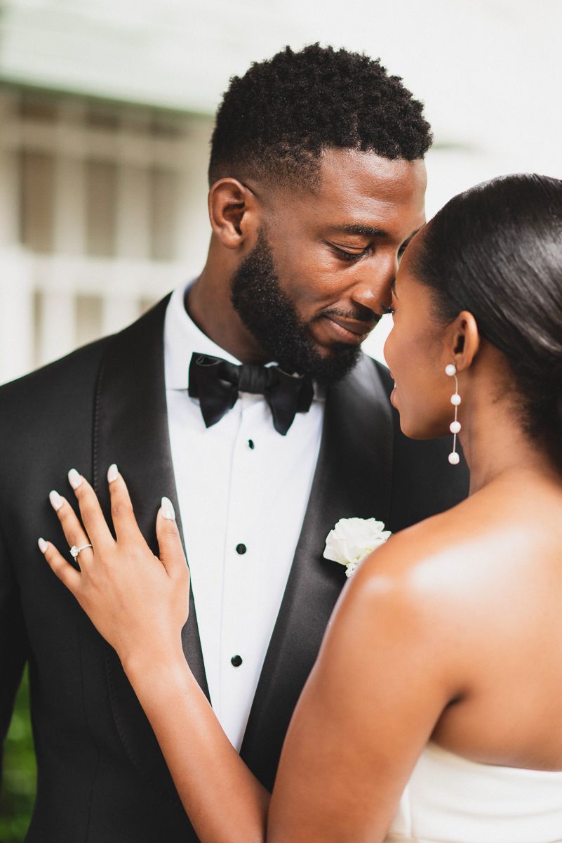 Elegant Black couple in wedding attire, groom in tuxedo with bow tie, bride in white dress with pearl earrings.