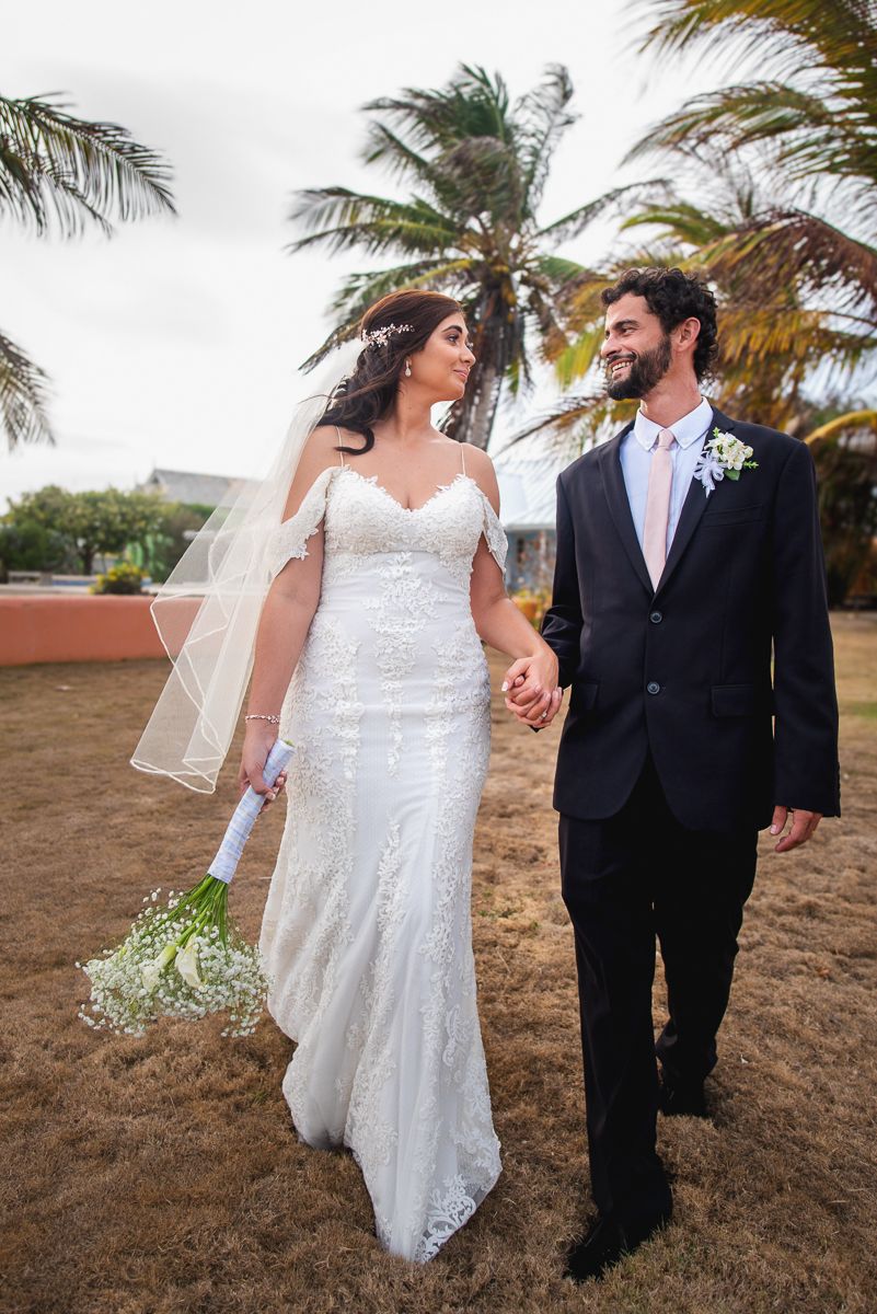 Wedding couple walking along a beach path with swaying palm trees in the tropical setting.