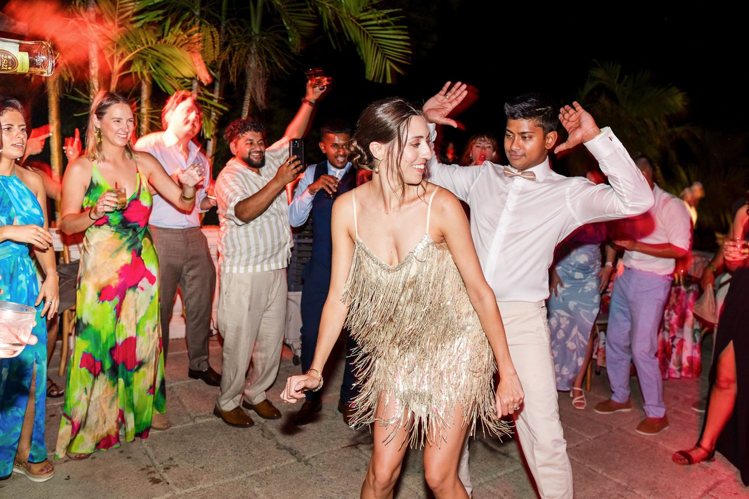 Lively crowd dancing and celebrating at a nighttime party with colorful lighting and festive atmosphere.