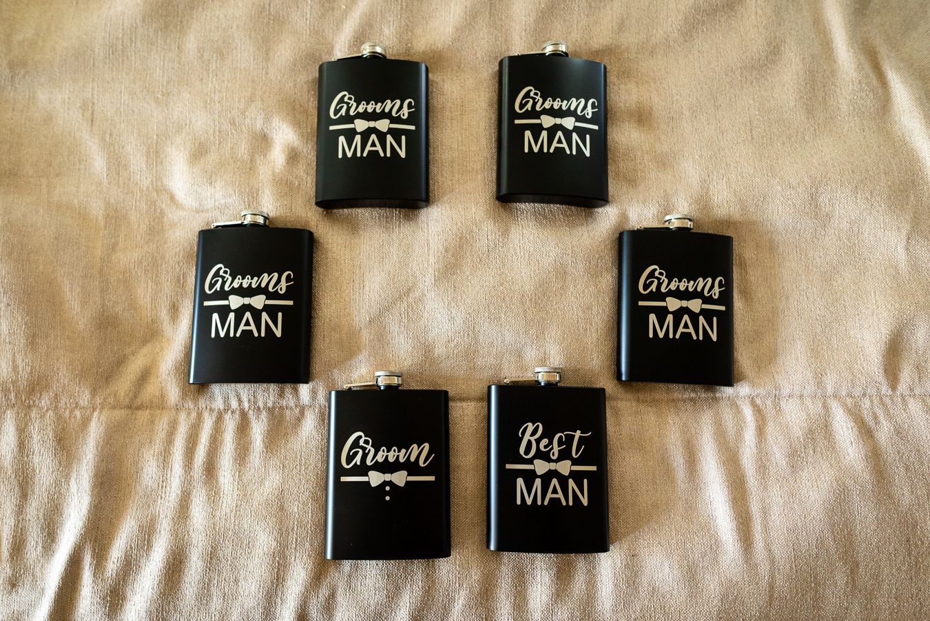 Multiple black flasks with 'Groom Man' labels arranged on a beige background.