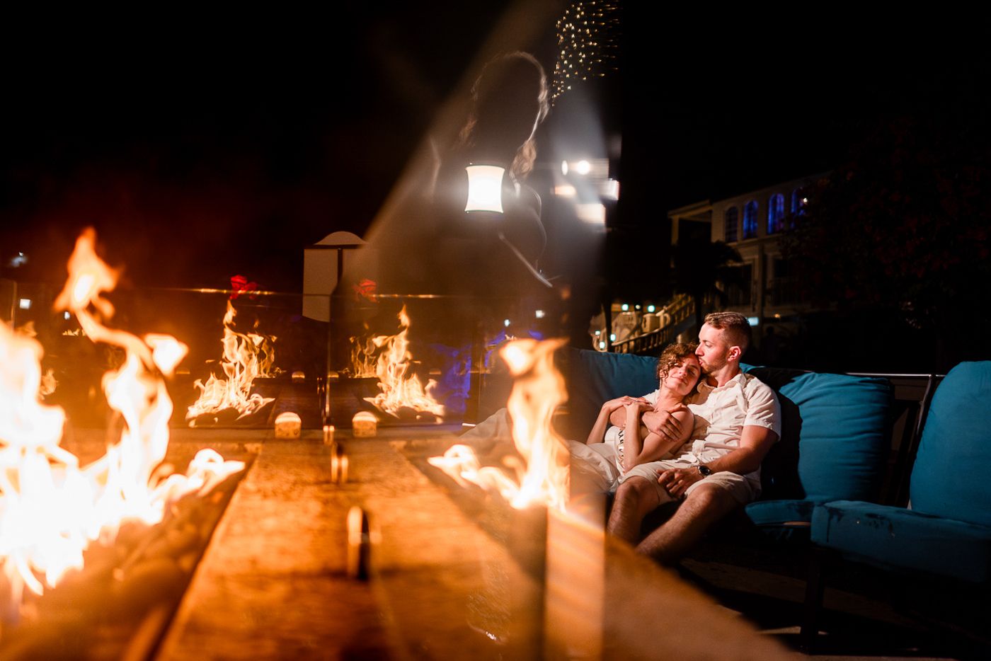 Romantic scene by firelight with couple lounging on blue outdoor furniture.