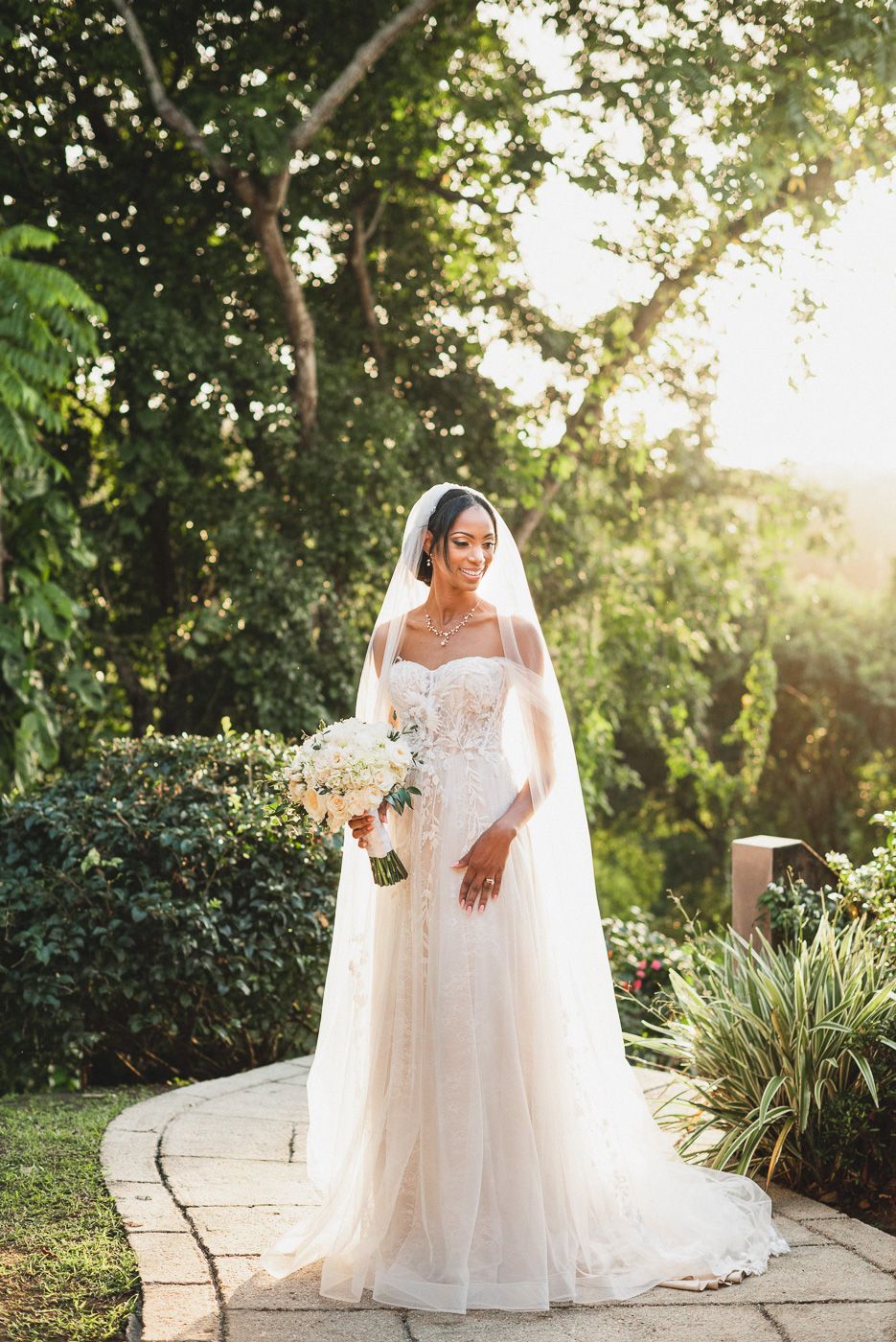A stunning bridal portrait in a garden setting with flowing white gown and floral bouquet.