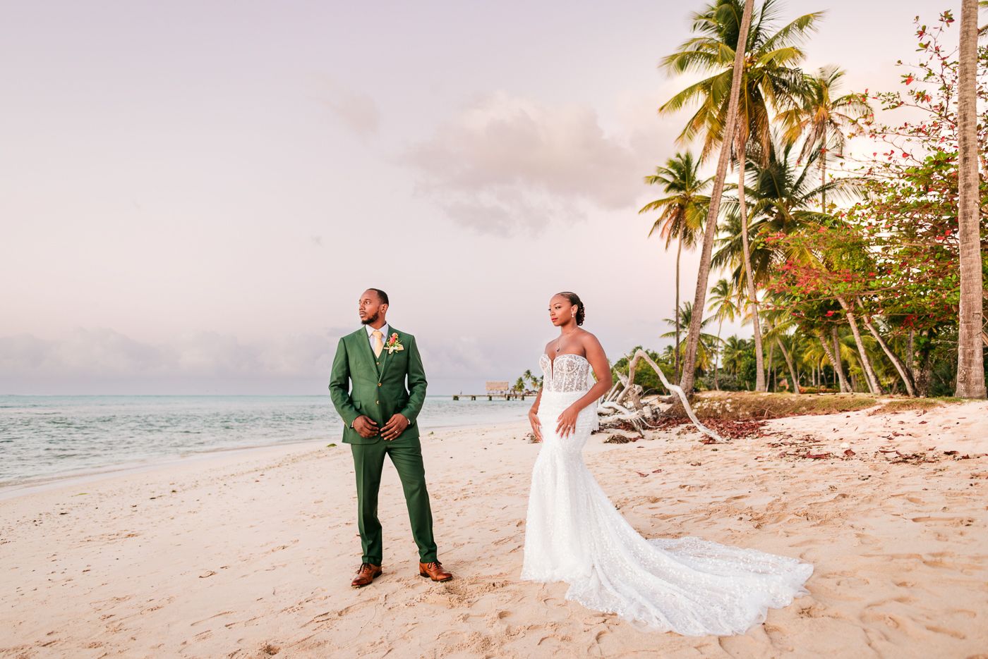 A couple poses for romantic wedding photos at sunset on a tropical beach with swaying palm trees and soft sand.