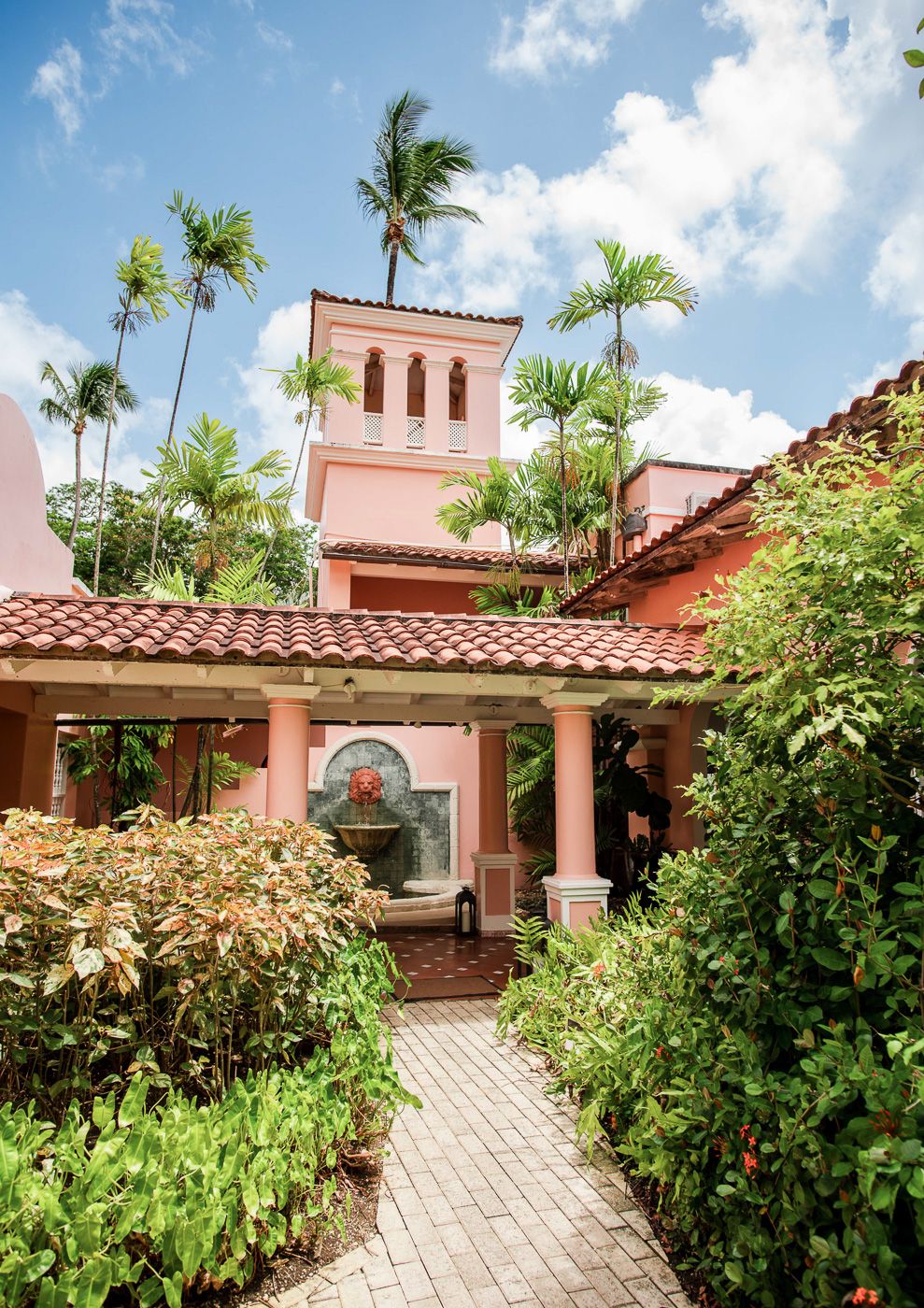 Spanish colonial style resort buildings with pink walls and terracotta roofs surrounded by palm trees.